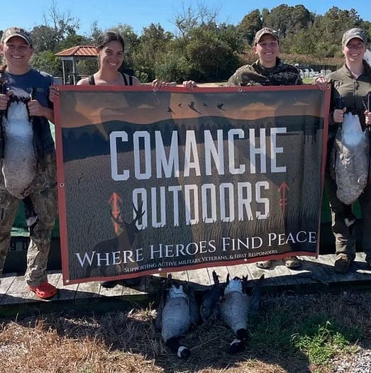 Participants holding a Comanche Outdoors banner behind a row of harvested geese