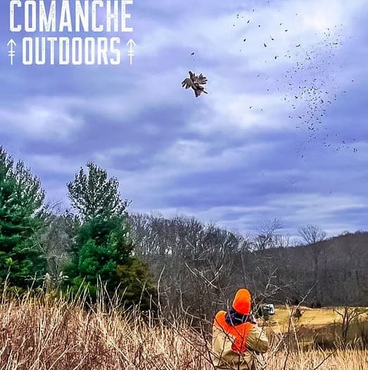 A shooter in blaze orange swinging on a flushing gamebird against the sky