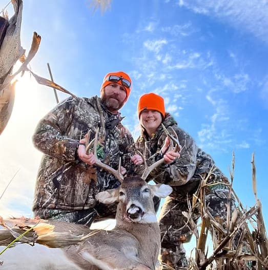 Two hunters in blaze orange with a whitetail buck