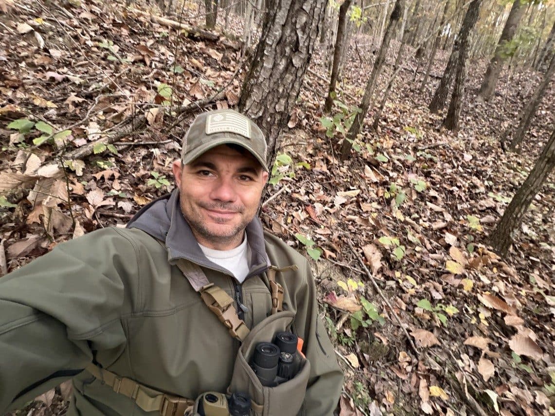 The author smiling in a selfie among autumn leaves and trees, binoculars in a chest pack.
