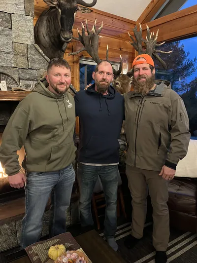 Hunters relax in a lodge under mounted deer heads.