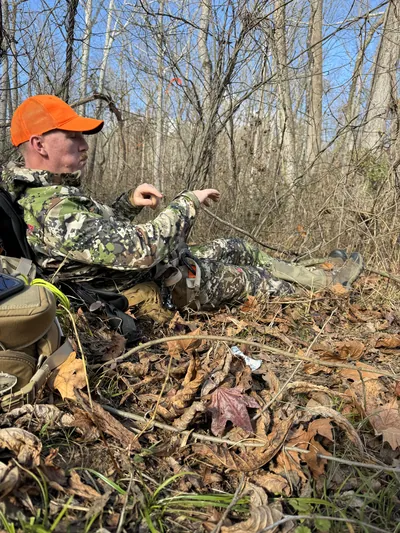 A hunter sits quietly among fallen leaves in autumn woods.