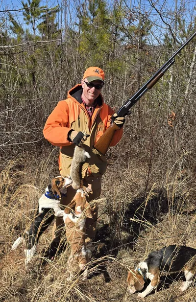 A hunter holds a rabbit with beagles at his feet.