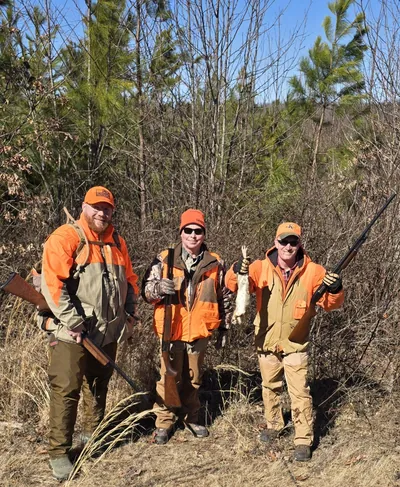 Three rabbit hunters stand among pine trees.