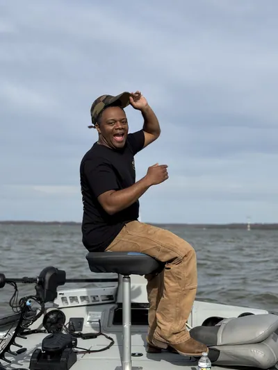 A man laughs and tips his cap on the deck of a bass boat.