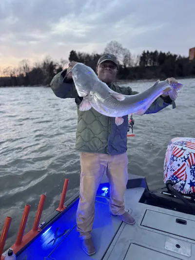 An angler holds a catfish at dusk.