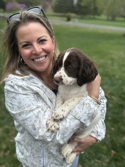 A woman smiles while holding a springer spaniel puppy.
