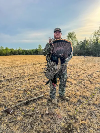 A turkey hunter holds his gobbler in a field at sunrise.