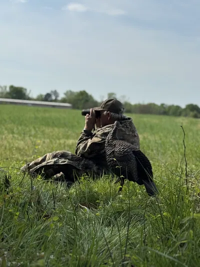 A hunter holds a turkey fan in tall grass.