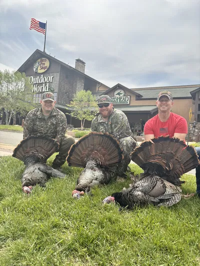Three hunters hold their turkeys outside a sporting goods store.