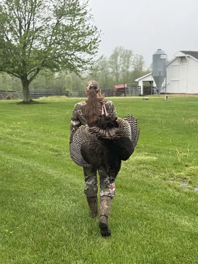 A turkey hunter walks across a farm field toward a silo.