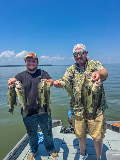 Two anglers laugh while holding up bass on a lake.