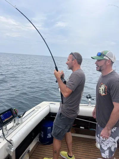 Two anglers watch a bent rod on a charter boat on open water.
