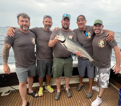 Five men in matching Comanche Outdoors shirts hold a king salmon on a boat deck.