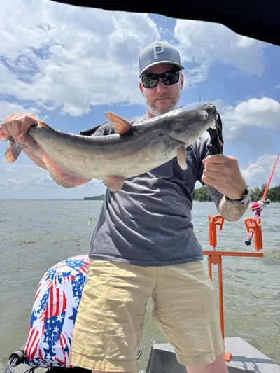 An angler holds a catfish on a boat, seen from a low angle.