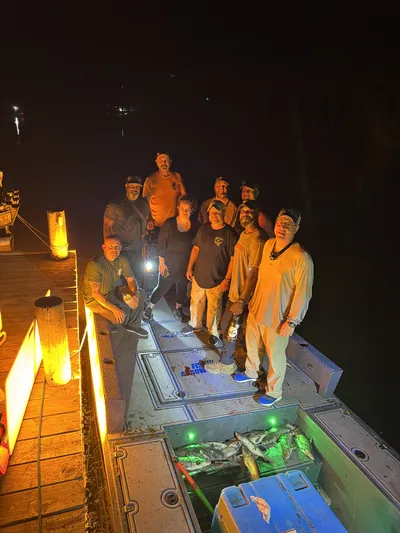 A bowfishing crew on a boat at night with their catch.