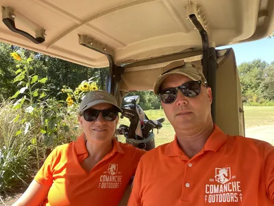 Golfers in orange Comanche Outdoors polos take a selfie in a golf cart.