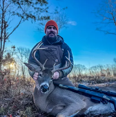 A hunter poses with a whitetail buck on a frosty morning.