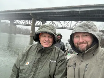 A hunter in a rain hood takes a selfie under a bridge.
