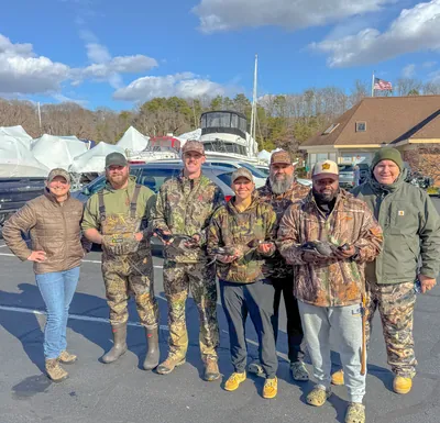 Seven hunters hold their ducks in a marina parking lot.
