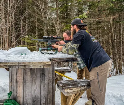 A hunter sights in a rifle at a snowy shooting bench.