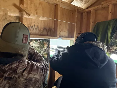 Hunters watch from inside a shooting house, seen from behind.
