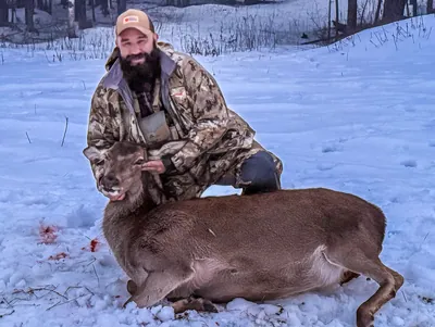 A hunter poses with a harvested hind in the snow.