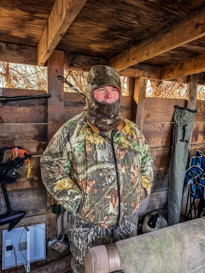 A hunter in a balaclava sits in a duck blind.