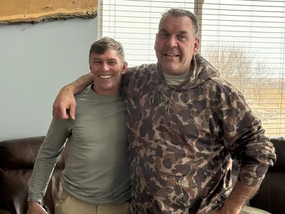 Two men stand arm in arm inside a lodge.