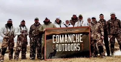 A snow goose hunting group stands behind the Comanche Outdoors banner.