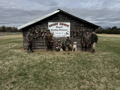 A hunting group gathers outside a preserve shed with ducks on the wall.