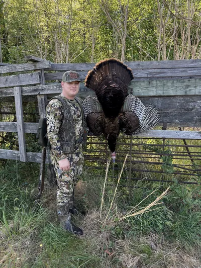 A gobbler hangs on a fence beside the hunter who took it.