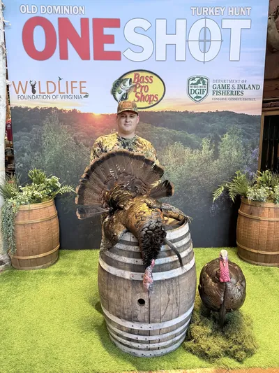 A hunter poses in front of a sponsor backdrop at a turkey hunting event.