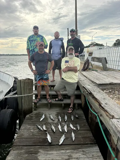 Six anglers stand on an old pier with their catch laid out.