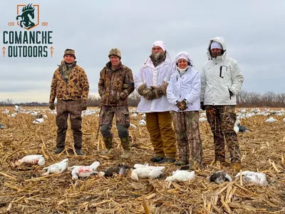 Hunters in white camouflage stand among snow goose decoys.