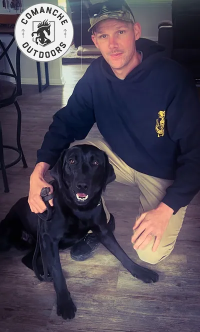 A handler kneels with a black Labrador.