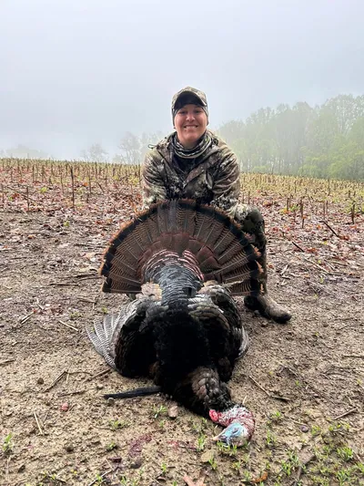 A hunter holds her gobbler with its tail fanned in a misty field.