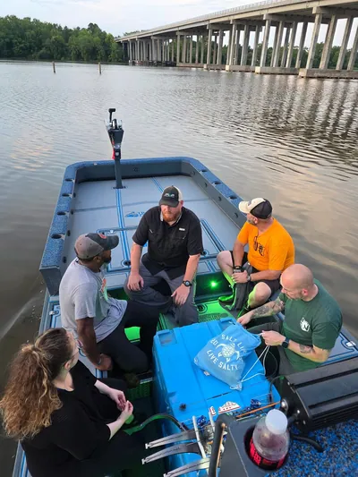 A bowfishing crew on a small boat at dusk, seen from above.