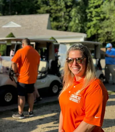 A smiling man in an orange Comanche Outdoors polo at the charity golf event.