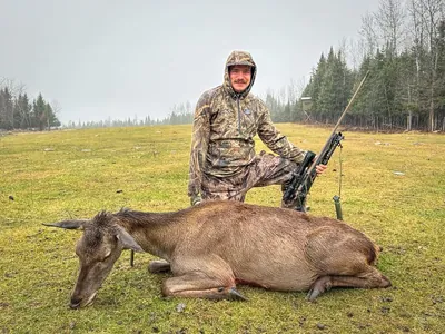 A hunter poses with a harvested hind on open grass.