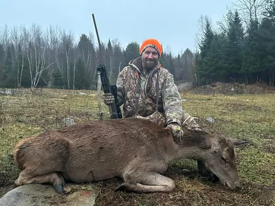 A hunter in a blaze orange beanie poses with a harvested hind.