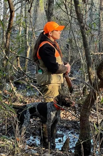 A hunter and a pointer walk through swampy woods.